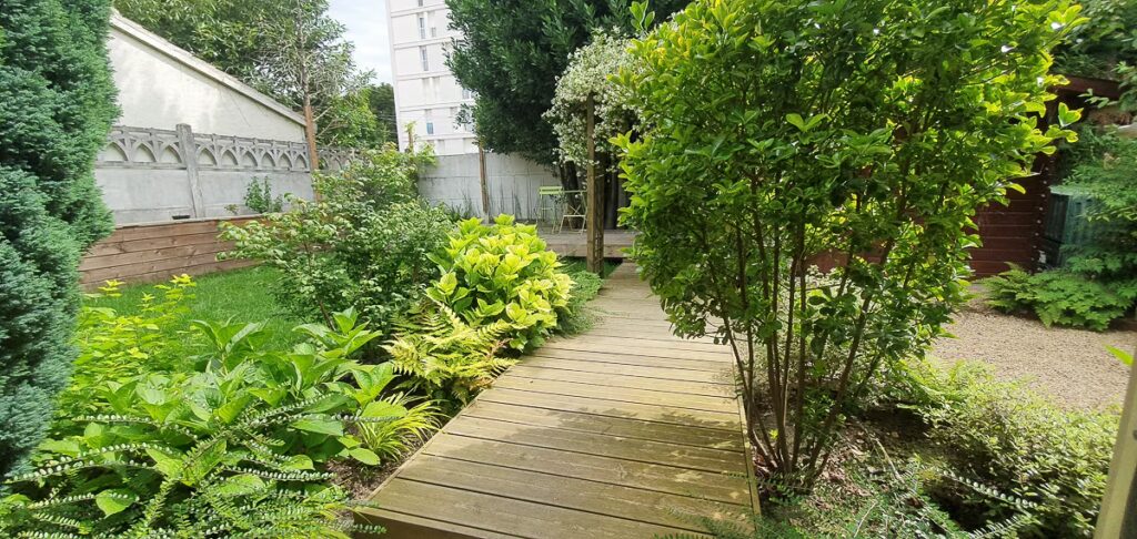 Cheminement en bois dans un jardin pavillonnaire à Villejuif (Val-de-Marne) entouré de plantations luxuriantes et d’arbustes