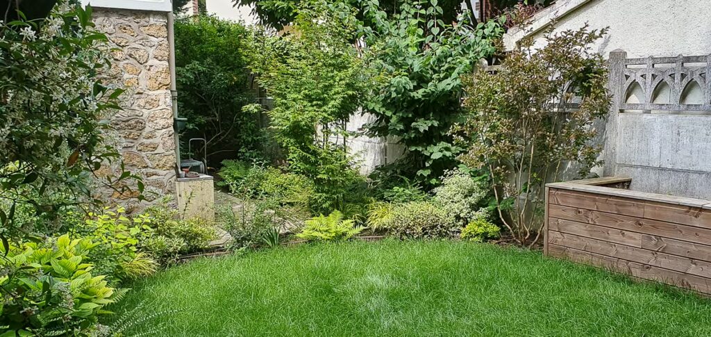 Pelouse bordée de massifs paysagers, arbustes et bardage en bois d'un espace potager dans un jardin de particulier à Villejuif (Val-de-Marne)